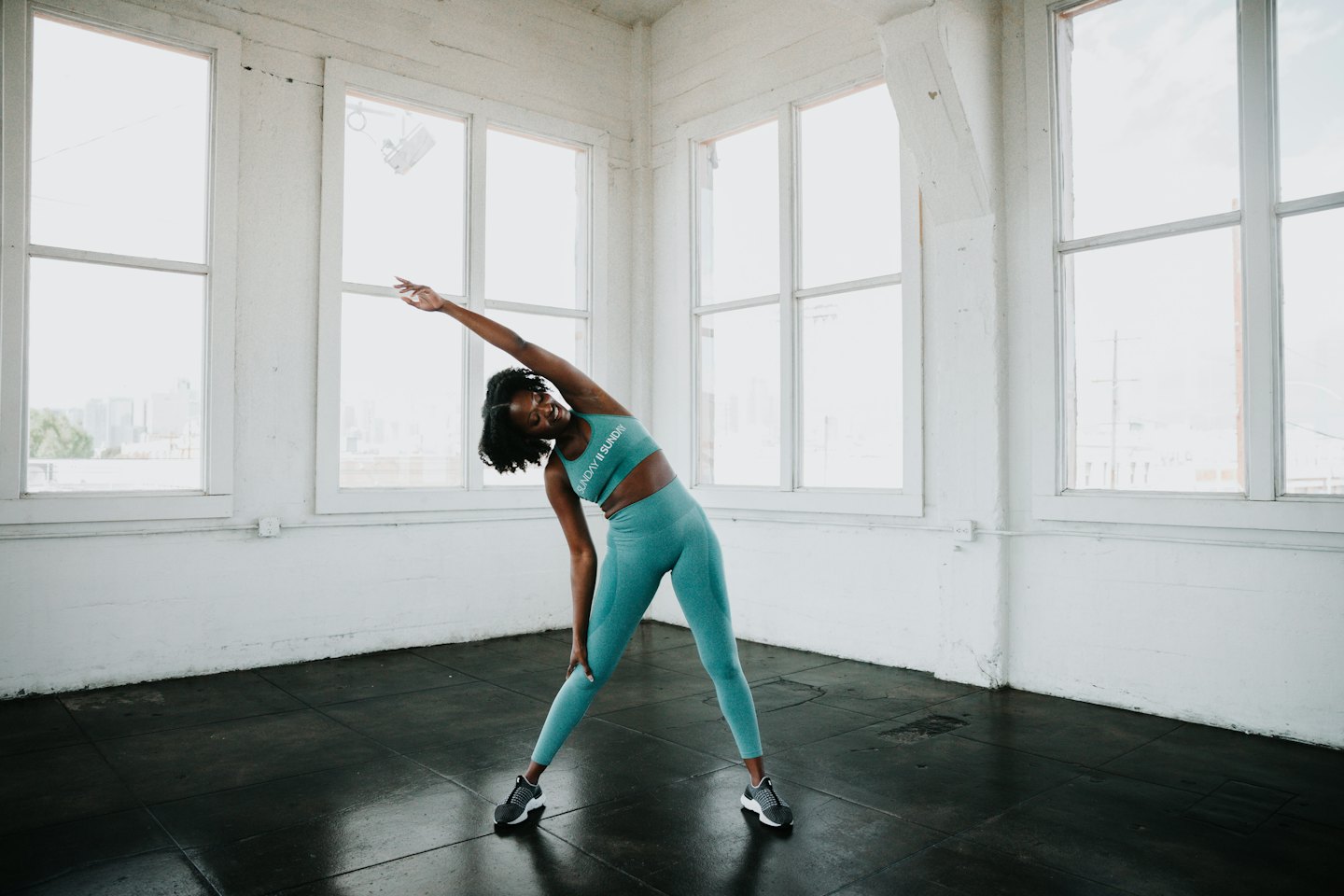 Woman in teal activewear smiling while side bending.