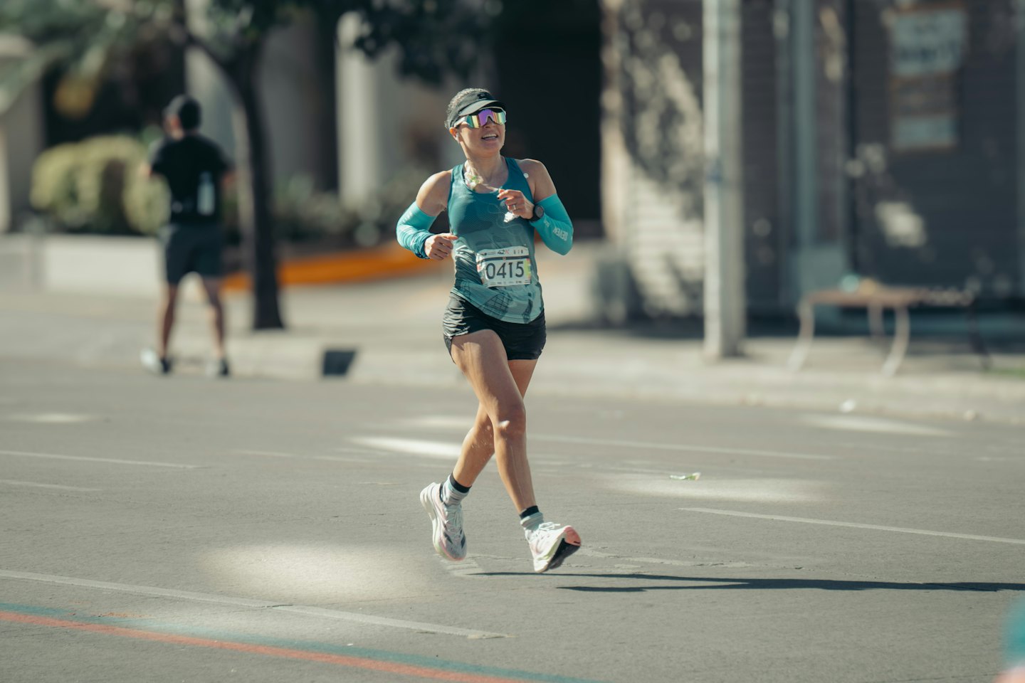 Woman in a teal tank top running a race.